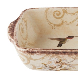 Puede incluir: Un plato para hornear de cerámica con fondo crema y diseño floral. El plato presenta un colibrí en vuelo y un borde marrón.