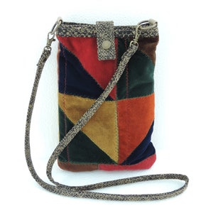 May include: A small, patchwork-style crossbody bag with a brown strap. The bag is made of different coloured fabrics, including red, orange, green, and brown. The bag has a flap closure with a button.