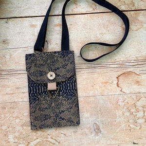 May include: A navy and beige crossbody bag with a snakeskin design. The bag features a flap closure with a wooden button and a beige strap. The adjustable strap is navy blue. The bag is on a wooden surface.