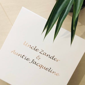 May include: White gift box with gold lettering that reads "Uncle Zander & Auntie Jacqueline"