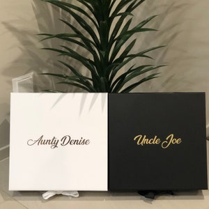 May include: Two gift boxes, one white with gold lettering that says "Aunty Denise" and one black with gold lettering that says "Uncle Joe".