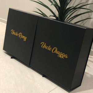 May include: Two black gift boxes with gold lettering. The box on the left says "Uncle Remy" and the box on the right says "Uncle Chugga".