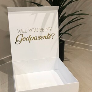 May include: White gift box with a gold inscription that reads "Will you be my Godparents?" The box is open and empty.