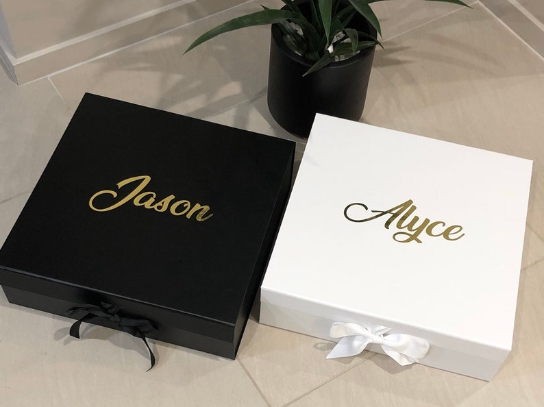 May include: Two personalized gift boxes, one black with the name "Jason" in gold lettering and one white with the name "Alyce" in gold lettering.
