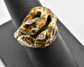 May include: A gold ring with two intertwined snakes, each with red eyes. The snakes are enameled in green, brown, and black.