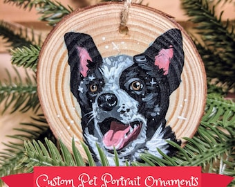 May include: A hand-painted wooden Christmas ornament featuring a portrait of a black, white, and brown dog with a pink tongue sticking out. The ornament is round and has a rustic wood grain texture. "Custom Pet Portrait Ornaments" is written in white cursive on a red ribbon.