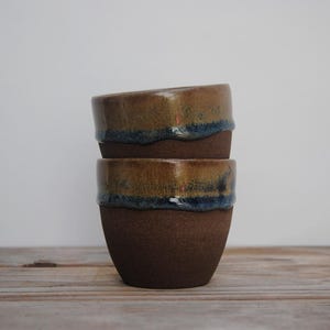 Puede incluir: Una taza de cerámica blanca con un asa negra y el texto "But First, Coffee" en negrita negra. La taza se encuentra sobre un fondo borroso, resaltando su diseño limpio.