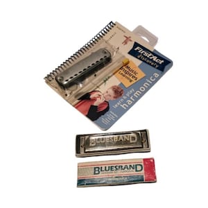 May include: An assortment of harmonicas and a learning kit. The kit includes a harmonica, a spiral-bound booklet, and a pencil. Two additional silver harmonicas are also visible, one with "BLUESBAND" engraved on it, and the other with a box.