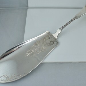 May include: A silver butter knife with an ornate handle and a twisted stem. The blade is engraved with a floral design.