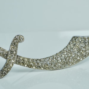 May include: A silver-toned brooch in the shape of a scimitar, completely covered in clear rhinestones.