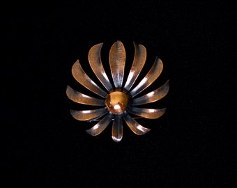 May include: A copper-toned metal brooch in the shape of a stylized flower with a round, gold-toned center.