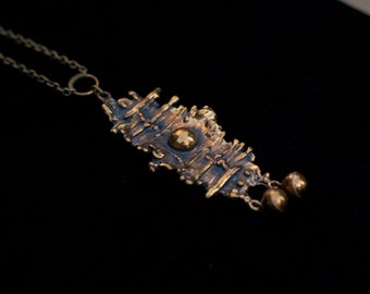 May include: A bronze pendant necklace with a textured, abstract design and two small, round accents. The pendant is attached to a chain.