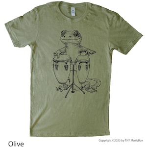 Puede incluir: Camiseta verde oliva con una ilustración en blanco y negro de un gecko tocando congas. El gecko sonríe y los tambores están sobre un soporte. El texto "Olive" está en la parte inferior izquierda. Copyright ©2023 by TNT MusicBox.