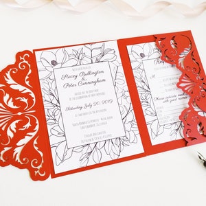 May include: A red tri-fold wedding invitation with intricate laser-cut designs. The invitation features floral illustrations and text, including names and a date. A black pen rests nearby.
