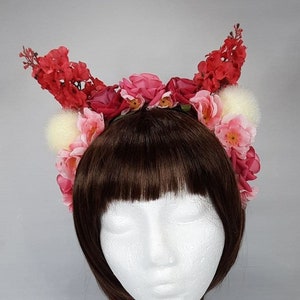 Könnte beinhalten: Eine rosa und rote Blumenkrone mit weißen Fell-Akzenten. Die Krone wird auf einem weißen Mannequin-Kopf mit braunen Haaren getragen.