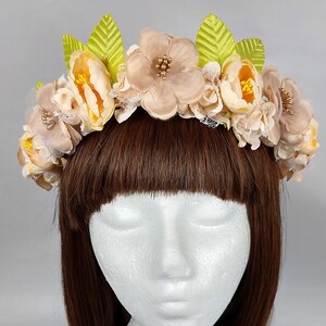 Könnte beinhalten: Eine braune Blumenkrone mit beigefarbenen und gelben Stoffblumen und grünen Blättern.