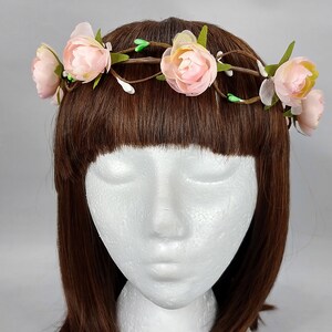Könnte beinhalten: Eine rosafarbene Blumenkrone mit grünen Blättern und einer braunen Rankenbasis. Die Krone wird auf einem Mannequin-Kopf mit braunen Haaren getragen.