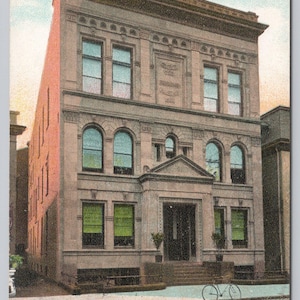 May include: Vintage postcard featuring the Odd Fellows Building in Wilkes Barre, PA. The multi-story building has arched windows, a detailed facade, and a prominent entrance. The postcard includes handwritten text and the building's name.