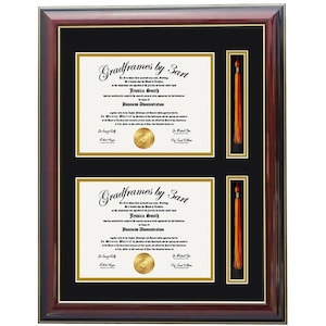 May include: A dark mahogany wood document frame featuring a black mat with gold trim. The frame holds two white diplomas with black text and gold seals, alongside two vertical rectangular slots displaying orange graduation tassels with gold cords.