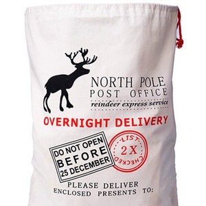 May include: A white canvas Santa sack with red and black text and a black reindeer silhouette. The text reads "North Pole Post Office, reindeer express service, Overnight Delivery, Do Not Open Before 25 December, List 2X Checked, Please Deliver Enclosed Presents To: If Undeliverable Return To: Santa Claus, North Pole."