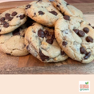 May include: A pile of freshly baked chocolate chip cookies on a wooden surface. The cookies are golden brown with visible chocolate chips. The image includes the text "Sweet Myrtle Bakery" and "Georgia Grown".