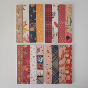 May include: A set of 10 decorative paper strips with a fall theme. The strips feature various patterns including plaid, polka dots, and floral designs. The strips also feature images of pumpkins, turkeys, and leaves. The text "Harvest, Thankful, Family, Memories, Love, Friends, Home" is printed on one of the strips.