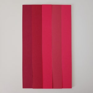 May include: Five vertical strips of paper in shades of red, from a deep burgundy to a bright pink.