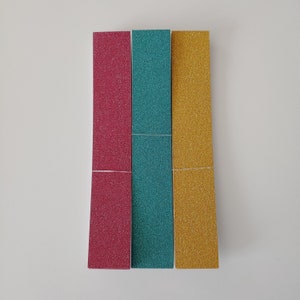 May include: Three glitter paper strips, one red, one teal, and one gold.