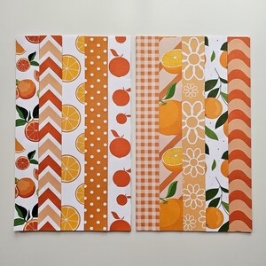 May include: Two rectangular sheets of patterned paper with an orange theme. Designs include orange slices, whole oranges, polka dots, chevrons, and floral patterns. The color palette is primarily orange, white, and peach.