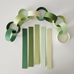 May include: A paper chain garland in shades of green, with individual links and vertical color swatches. The garland links are in various shades of green, from dark to light. The vertical swatches are in a gradient of green.