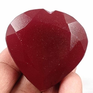 Può includere: Una gemma sfaccettata a forma di cuore, di colore rosso intenso. La gemma ha molteplici superfici piatte che riflettono la luce, creando un effetto scintillante. La forma a cuore è ben definita, con una leggera rientranza nella parte superiore.