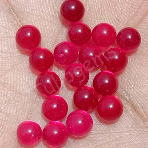 May include: A collection of fifteen small, round, translucent red beads with a smooth, polished surface. Each bead features a consistent spherical shape and a vibrant, deep red color that catches the light, creating subtle highlights on the surface.