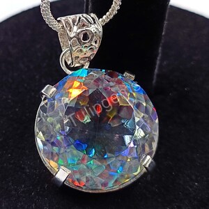 May include: A silver pendant necklace featuring a large, faceted, round gemstone. The gemstone displays a spectrum of colors, including blue, green, and yellow, due to light refraction. The pendant is suspended from a delicate silver chain, showcasing a detailed bail.