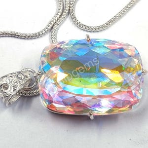 May include: A large, iridescent gemstone pendant with a faceted, rectangular cut. The pendant is suspended from a silver chain. The gemstone displays a spectrum of colors, including blues, greens, and yellows. The pendant is a statement piece of jewelry.