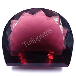 May include: A faceted, semi-circular gemstone with a deep burgundy hue. The gem has a flat base and a domed top, with multiple facets creating a sparkling effect. The text "Tulipgems" is printed on the surface of the gem.