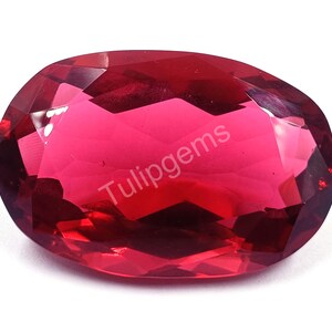 May include: A faceted, oval-shaped gemstone in a vibrant shade of red. The gem has a polished surface with multiple facets that reflect light. The text "Tulipgems" is visible on the surface. This gemstone is suitable for jewelry making.