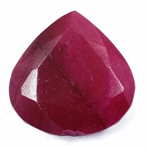 Pode incluir: Uma pedra preciosa de rubi facetada em forma de coração. A gema é de uma cor vermelha profunda e saturada, com múltiplas facetas que refletem a luz. A forma é um coração arredondado, com uma ponta e um topo largo e curvo. A pedra preciosa está sobre um fundo branco.