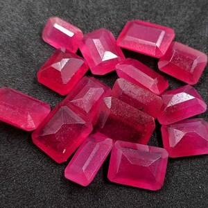 Pode incluir: Uma coleção de pedras preciosas facetadas, de formato retangular, vermelho escuro. As pedras têm uma superfície polida e reflexiva e estão dispostas sobre um fundo escuro. As pedras são de vários tamanhos e formas, com cortes retangulares e trapezoidais.