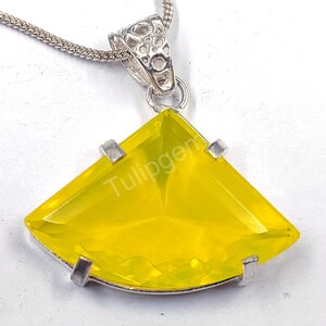 May include: A silver pendant necklace featuring a bright yellow, fan-shaped gemstone. The gemstone is set in a silver frame and is suspended from a delicate silver chain. The text "Tulipgem" is visible on the gemstone.