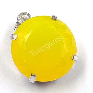 May include: A faceted, round, bright yellow gemstone pendant with a silver-colored bail and prongs. The text "Tulipgems" is printed on the gemstone. The pendant is set against a white background.