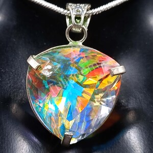 May include: A silver pendant necklace featuring a large, triangular, iridescent gemstone. The gemstone displays a vibrant array of colors, including blue, red, yellow, and green. The pendant is held by silver prongs and hangs from a silver chain.