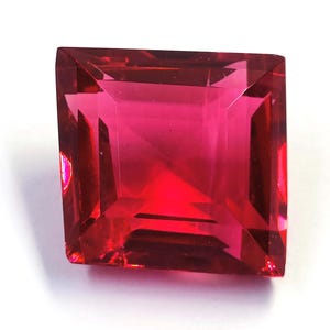 Op de afbeelding: Een vierkant geslepen, gefacetteerde edelsteen in een levendige, dieprode tint. De facetten van de edelsteen reflecteren licht, waardoor een schitterende weergave ontstaat. De edelsteen staat tegen een witte achtergrond.