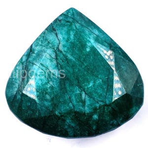 Puede incluir: Una gema facetada en forma de pera, de un profundo tono verde esmeralda. La gema presenta vetas internas y reflejos de luz, con el texto "lipgems" visible. La piedra está sobre un fondo blanco.