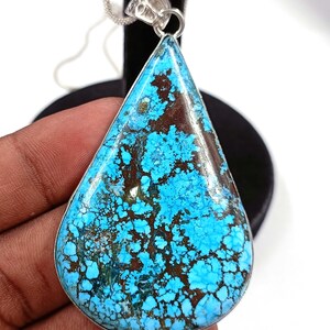 May include: A large, teardrop-shaped pendant with a vibrant turquoise stone. The stone has a matrix of brown and blue-green hues, set in a silver-colored metal frame. A silver chain is attached to the pendant.