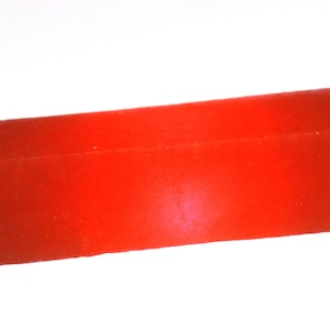 May include: A solid, rectangular, red object with a slightly rough texture. The object is a vibrant shade of red and appears to be made of a solid material. The shape is a simple, elongated block.