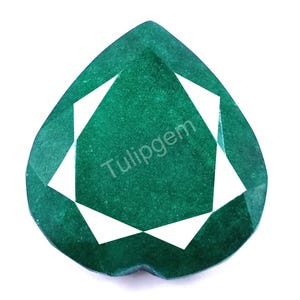Puede incluir: Una gema de esmeralda facetada en forma de corazón con un tono verde oscuro. La gema presenta facetas geométricas blancas y el texto "Tulipgem" en blanco. La gema está sobre un fondo blanco.