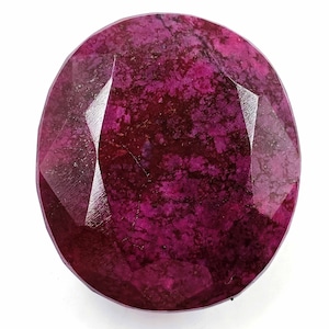 Può includere: Una gemma di rubino sfaccettata, di forma ovale. La gemma è di un colore rosso intenso e ricco, con un aspetto leggermente screziato. Le sfaccettature catturano la luce, creando un effetto scintillante. La gemma è su sfondo bianco.