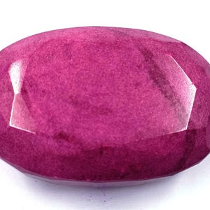 Puede incluir: Una gema de rubí facetada, de forma ovalada. La gema es de un color rojo-rosado intenso y saturado, con una superficie pulida. Las facetas crean un juego de luces y sombras.