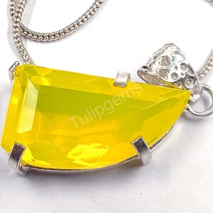 May include: A silver necklace featuring a large, bright yellow gemstone pendant. The pendant is a rectangular shape with a faceted surface, set in a silver bezel. The necklace chain is a delicate silver link.