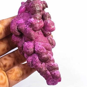 May include: A raw, unpolished mineral specimen featuring a vibrant magenta and deep purple coloration. The stone has a botryoidal, clustered texture with rounded, bulbous formations and a crystalline, granular surface throughout its structure.